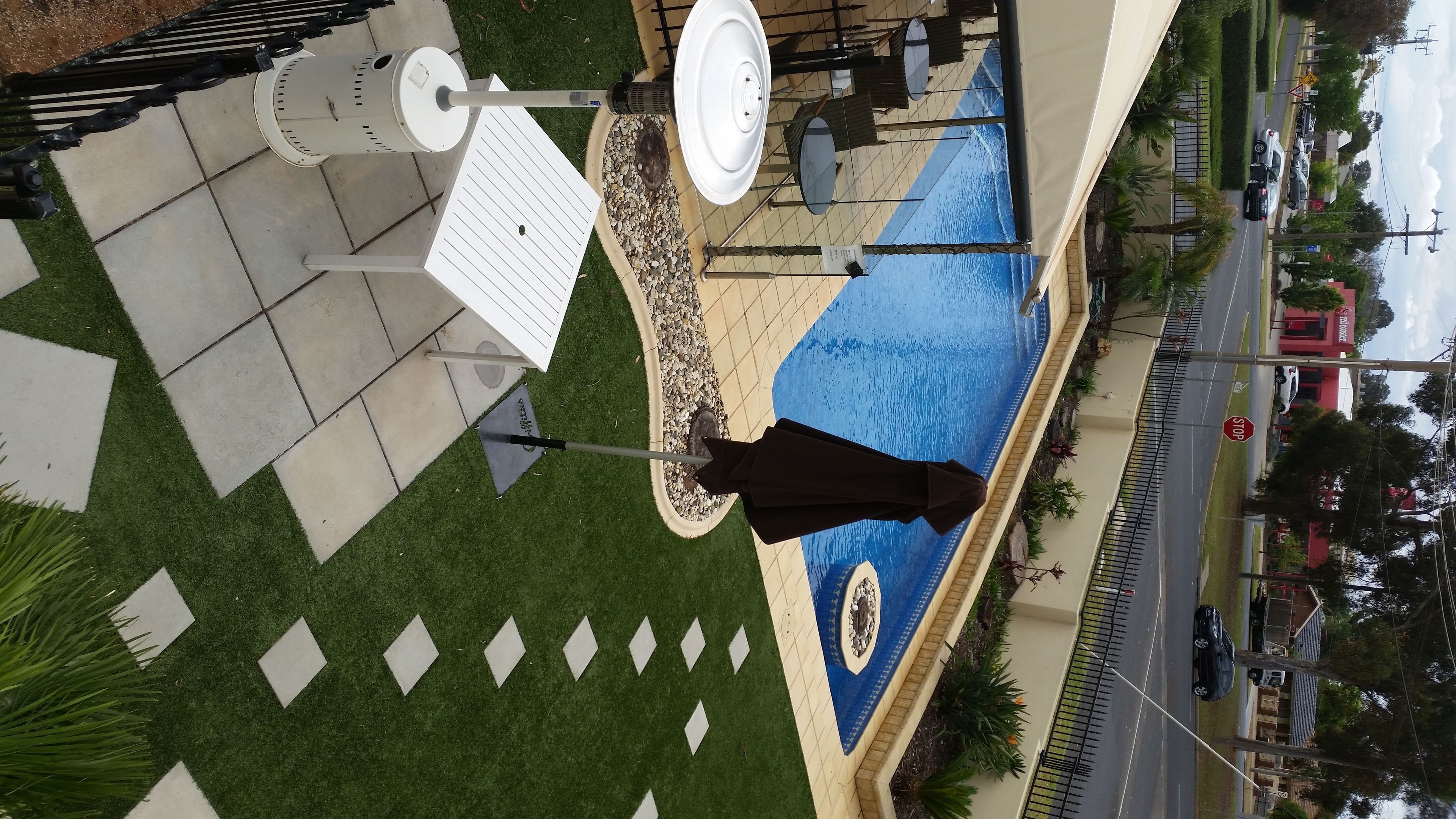 An aerial view of a pool area with a geometric tile pattern, a white table, and a black umbrella.