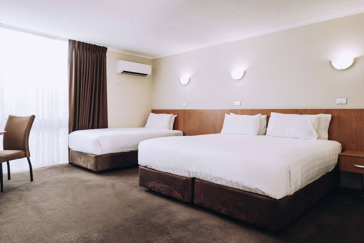 A hotel room with two beds, a chair, and a nightstand.