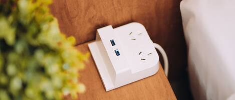 A white power strip on a wooden surface with a plant to the left.