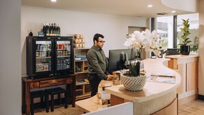 Un homme travaille derrière un comptoir dans un bureau moderne. On y voit un réfrigérateur rempli de boissons, un ordinateur et une orchidée en pot.