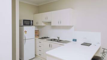 Una cocina compacta con armarios blancos, microondas, refrigerador, pileta y una pequeña mesada.
