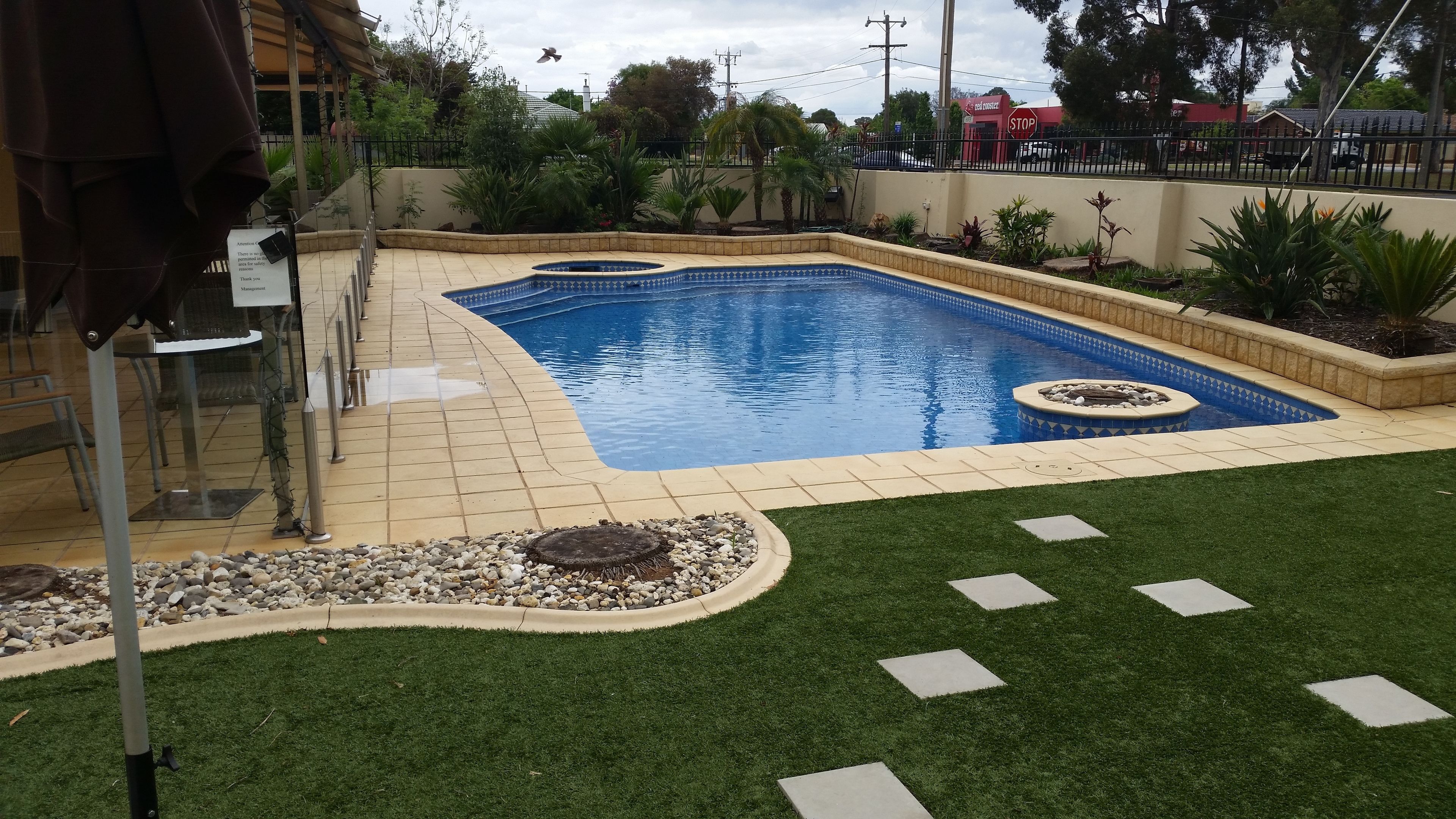 A swimming pool with a tiled deck, surrounded by a grassy area and a stone border.