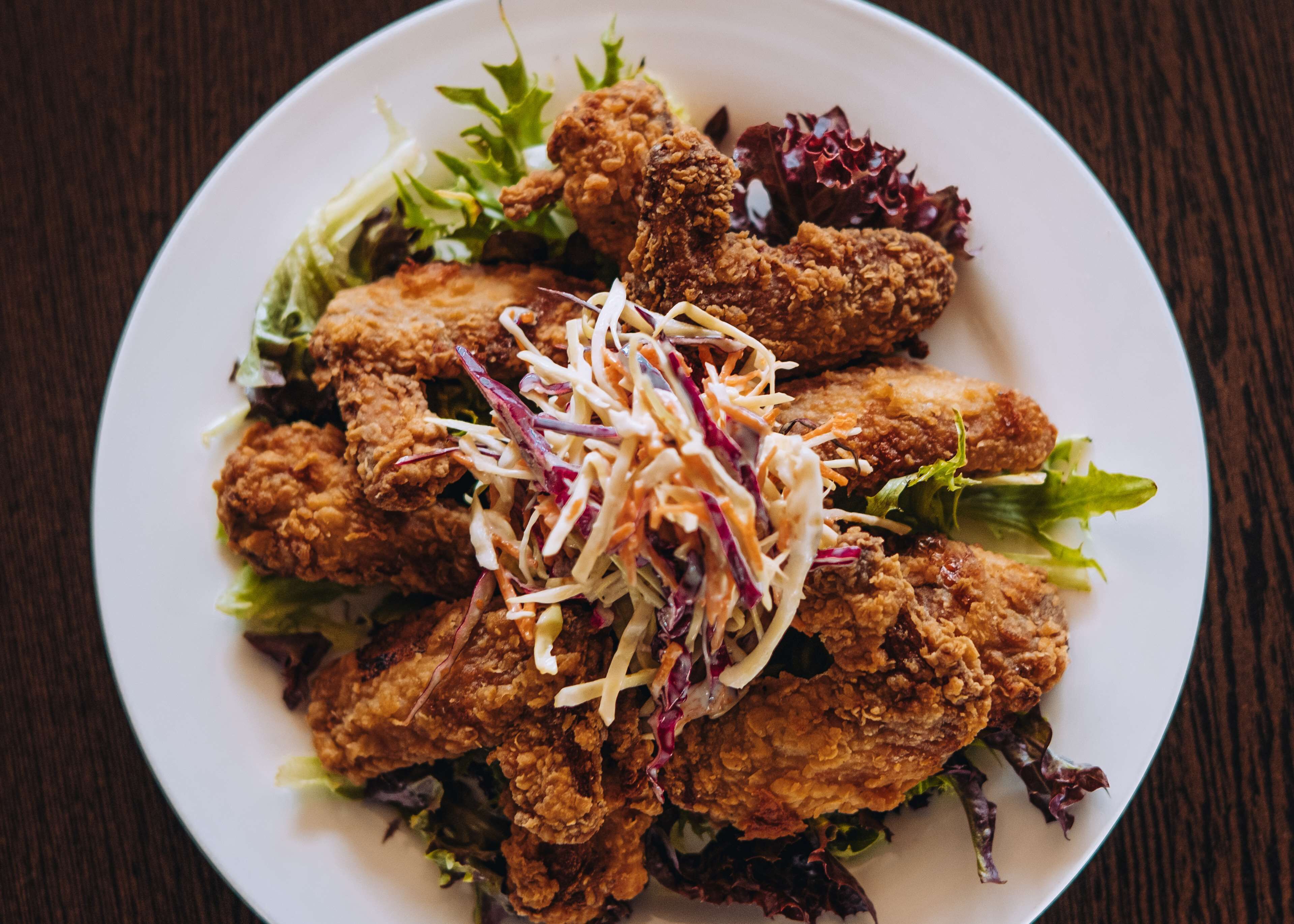 Un plato de pollo frito con ensalada de col y hojas verdes mezcladas.