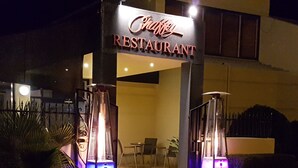 L’entrée d’un restaurant, avec une enseigne, deux structures illuminées et des tables à l’extérieur.