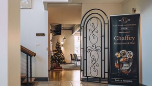 Un hall d’hôtel avec un escalier, un sapin de Noël, un comptoir d’accueil et une affiche pour le restaurant-bar Chaffey.