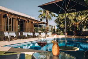 A glass of red wine and a tropical drink on a table by a poolside with a palm tree and a building in the background. - Best Western Chaffey Motor Inn (Mildura)