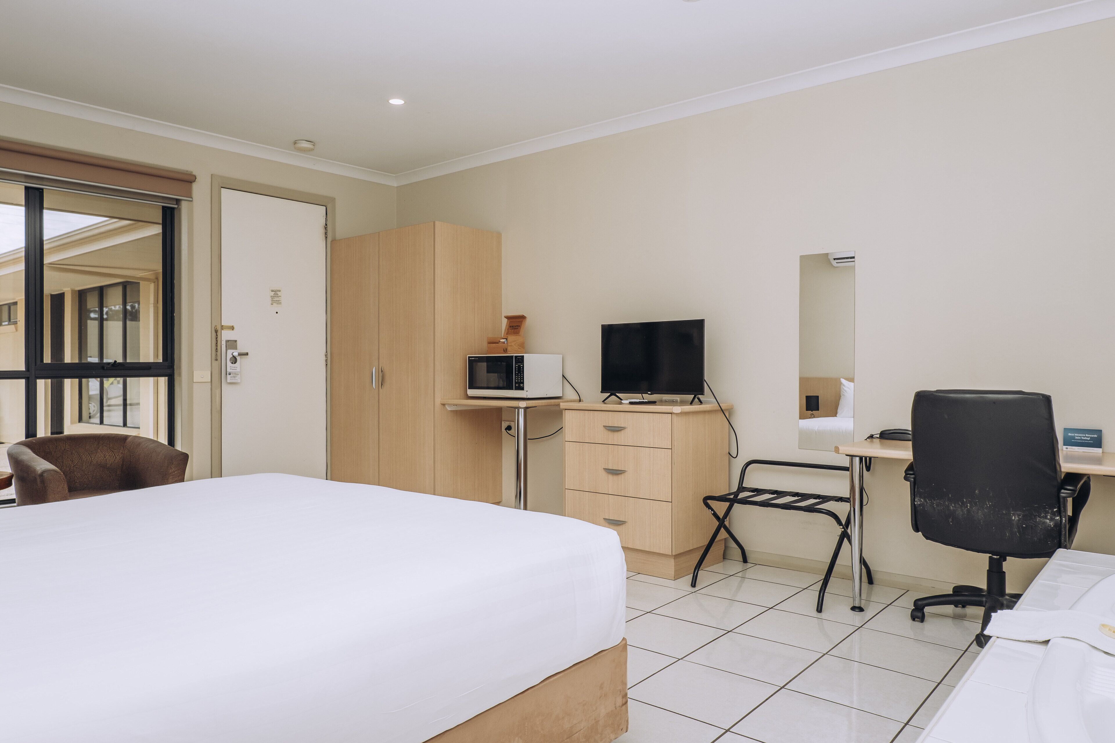 Une chambre d’hôtel équipée d’un lit, d’un bureau, d’une chaise, d’un four à micro-ondes, d’une télévision et d’une armoire.