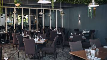 Un restaurante con varias mesas y sillas, plantas colgantes e iluminación colgante.