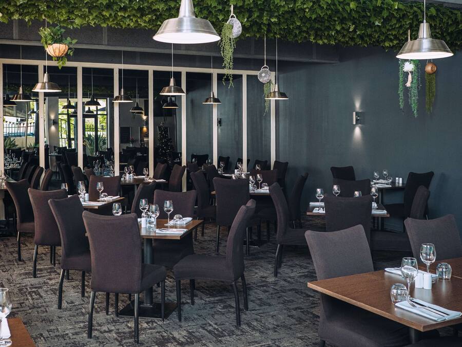 Un restaurante con varias mesas y sillas, plantas colgantes e iluminación colgante.