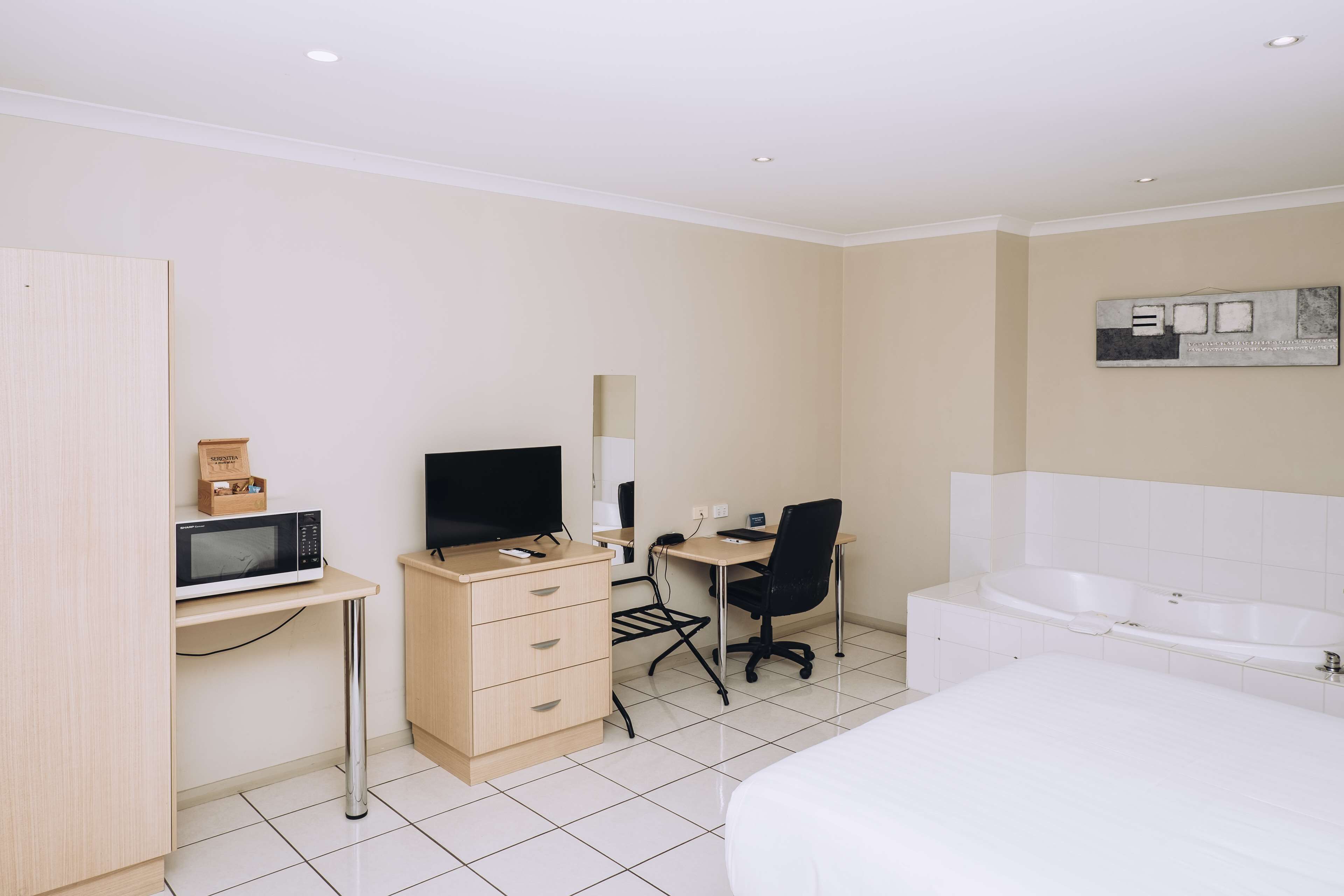 Una habitación de hotel con cama, escritorio con computadora, silla, microondas y bañera.