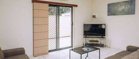 Una sala de estar con televisor, sofá y puerta corrediza de vidrio.