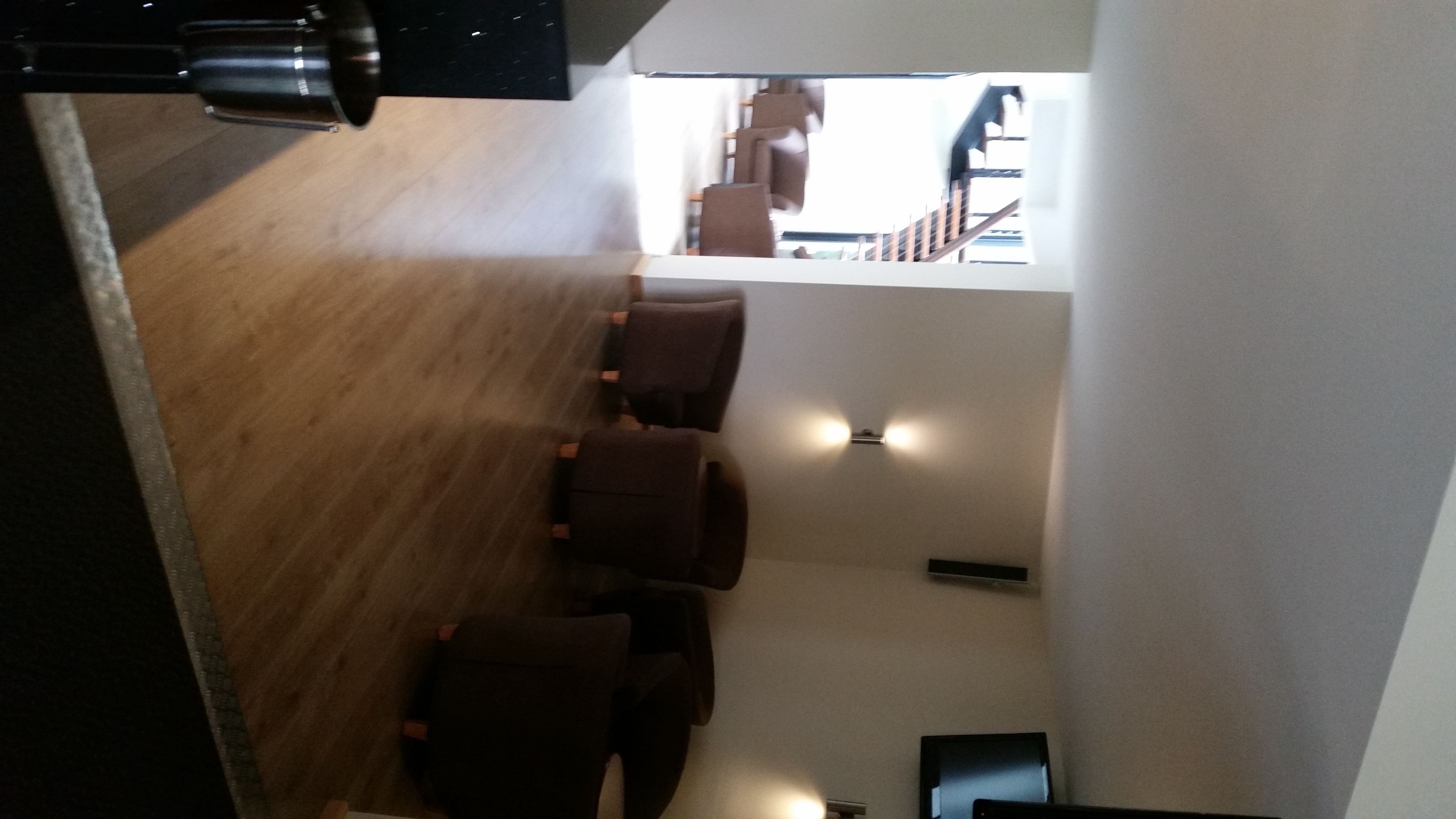 A modern interior with a wooden floor, several dark-colored chairs, and a staircase leading to an upper level.
