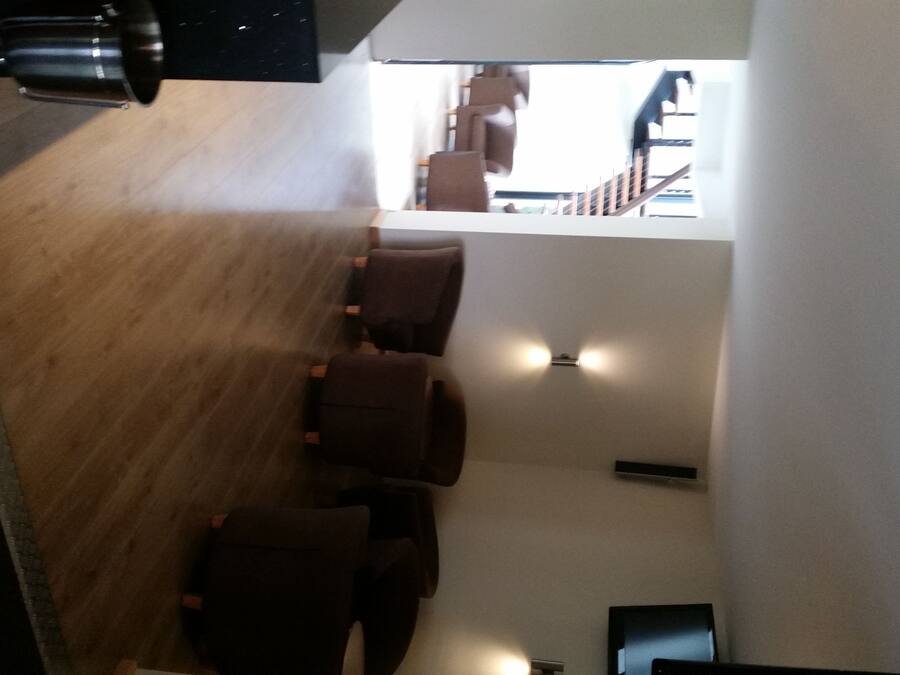 A modern interior with a wooden floor, several dark-colored chairs, and a staircase leading to an upper level.