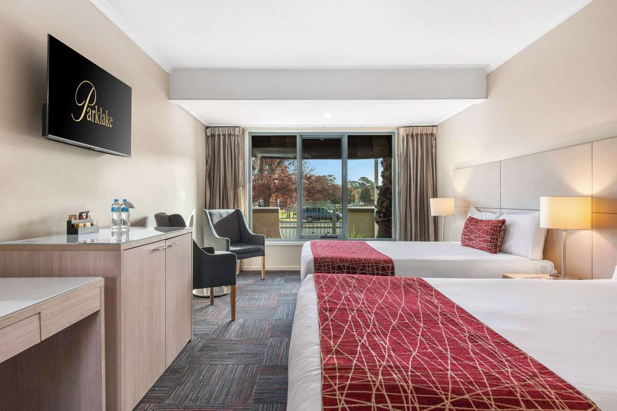 Habitación de hotel con escritorio, dos camas, una silla, televisor y vistas al exterior.