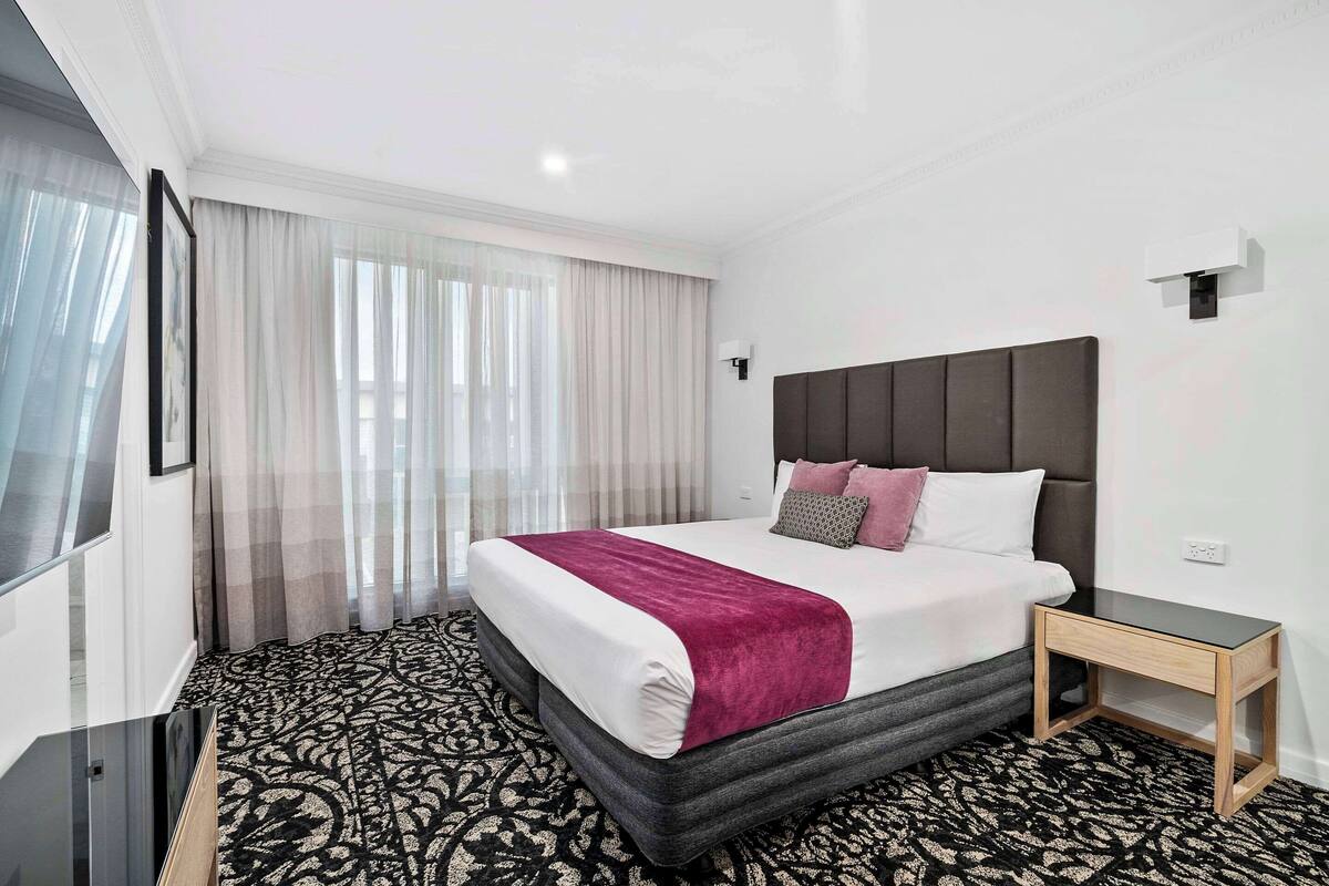 Habitación de hotel con una cama grande, una mesita de noche, un televisor de pantalla plana y una alfombra estampada.