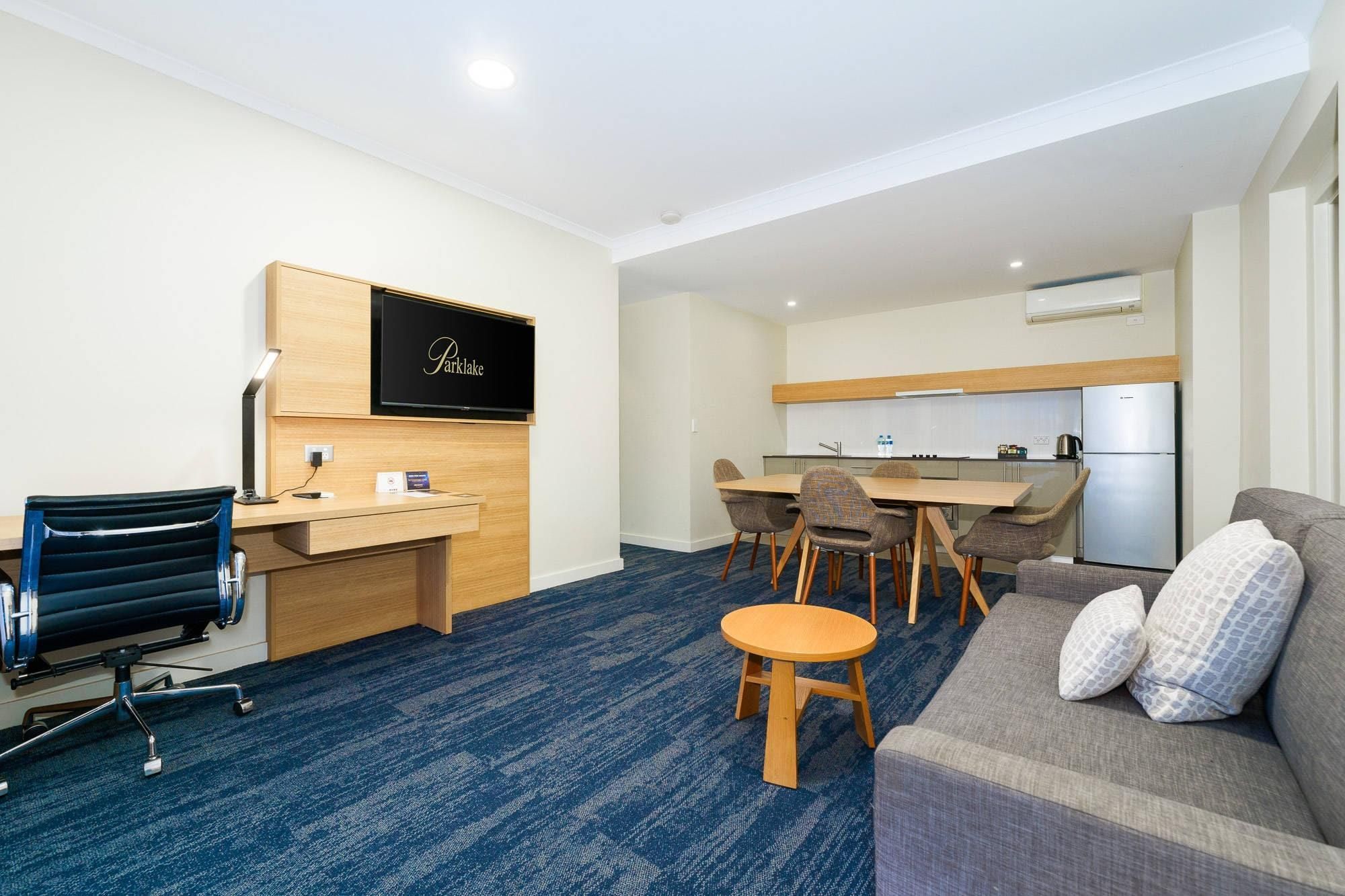 Una habitación de hotel con escritorio, sofá, una mesita redonda, televisor y kitchenette.