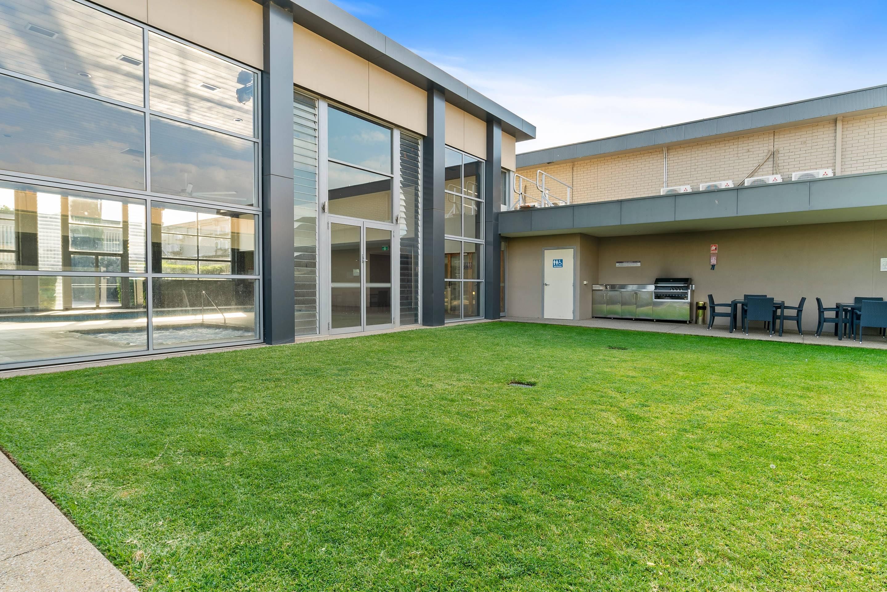 A modern building with large glass windows, a grassy courtyard, and outdoor seating.