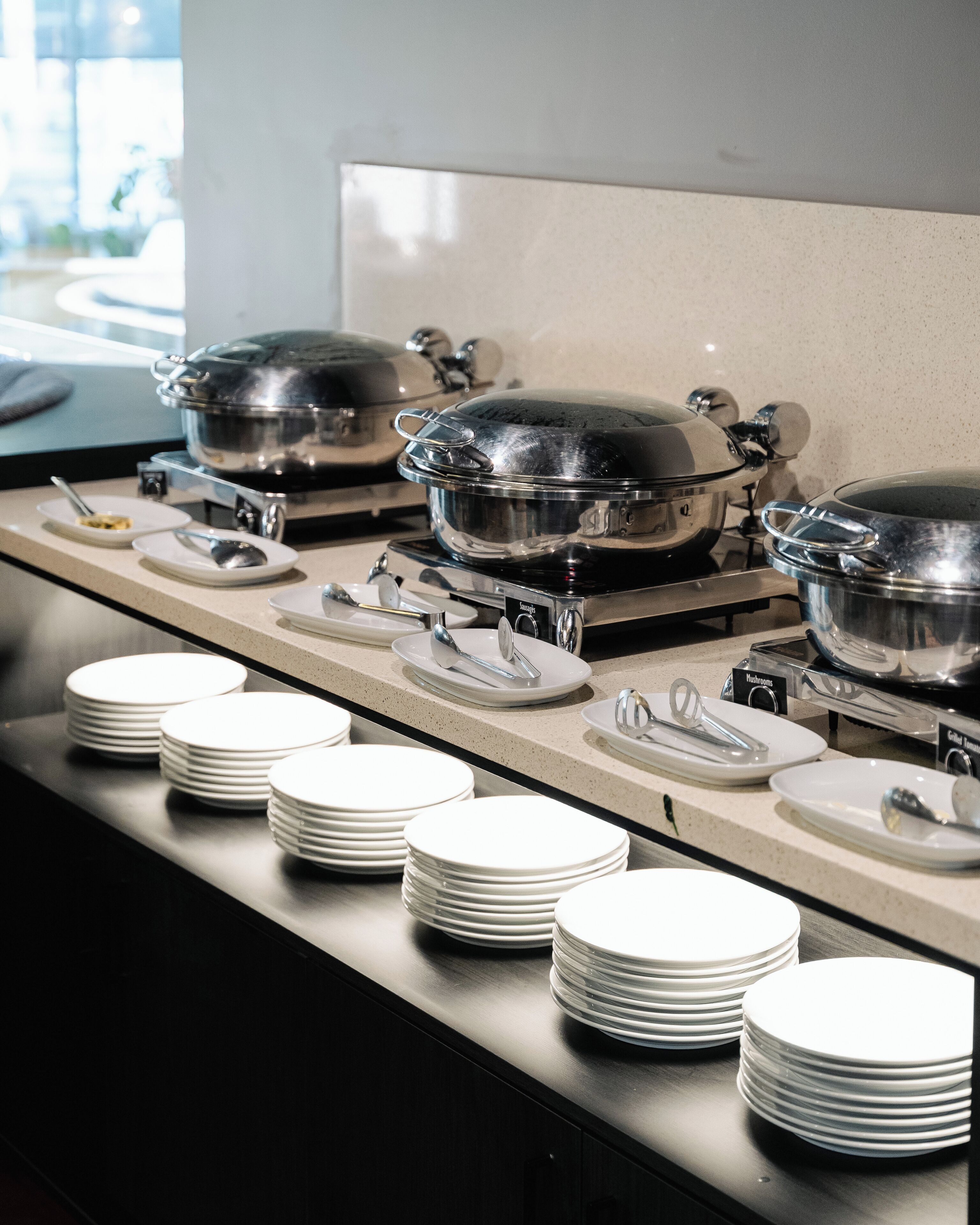 Disposição de buffet com várias estações de serviço, cada uma equipada com uma panela grande e diversos utensílios.