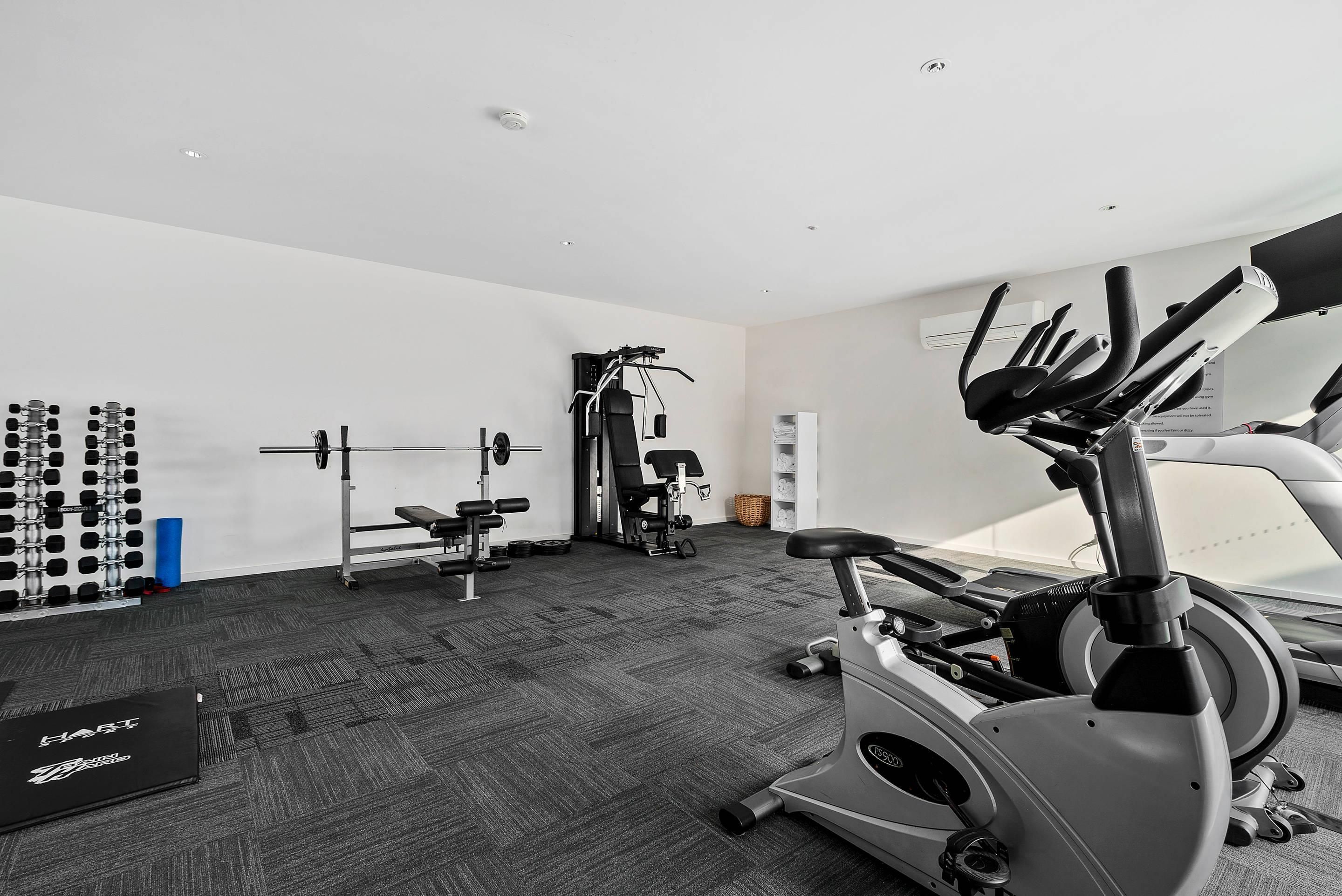 Uma academia com diversos equipamentos de exercícios, incluindo esteira, banco de musculação e pesos livres.