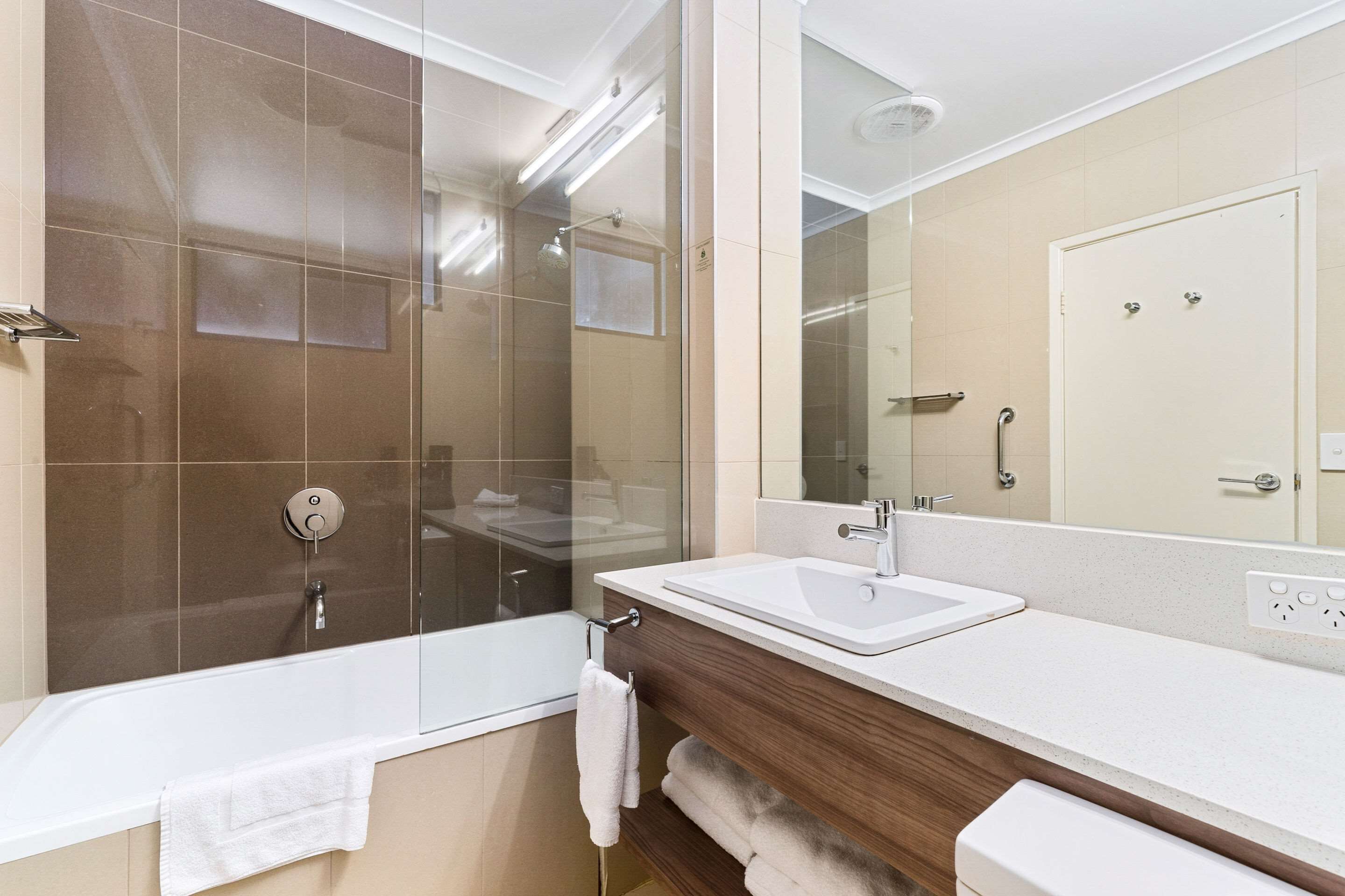 A modern bathroom with a glass-enclosed shower, a white sink, and a large mirror.