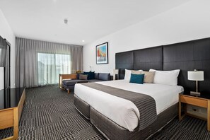 A hotel room with a large bed, a sofa, a desk, and a painting on the wall.