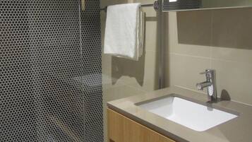 Un baño moderno con un lavamanos grande, un espejo y una zona de ducha con puerta de cristal.