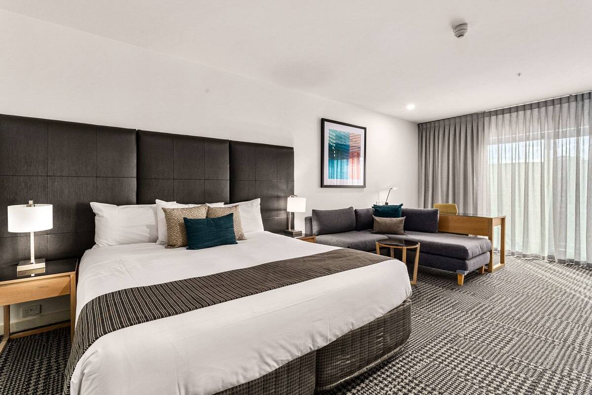 Una habitación de hotel moderna con una cama grande, un sofá, una mesita y una silla.