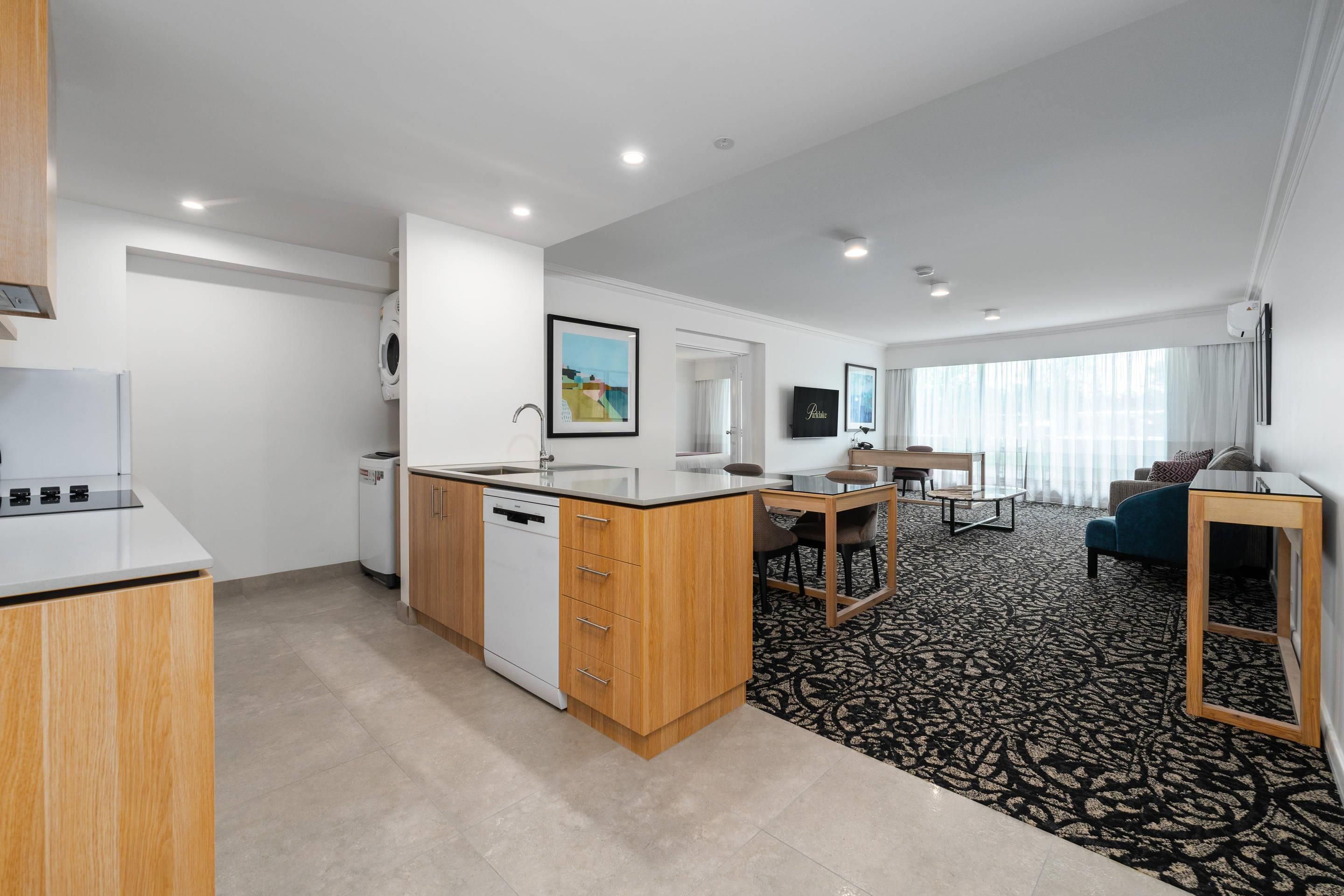 A modern kitchen with a dishwasher, a dining area with a table and chairs, and a living room with a sofa and a TV.