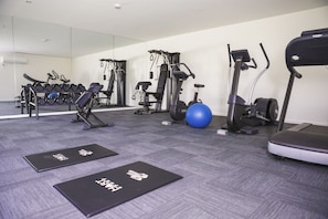 Une salle de sport équipée de matériel d’exercice, avec un ballon d’exercice bleu et des tapis noirs sur le sol.