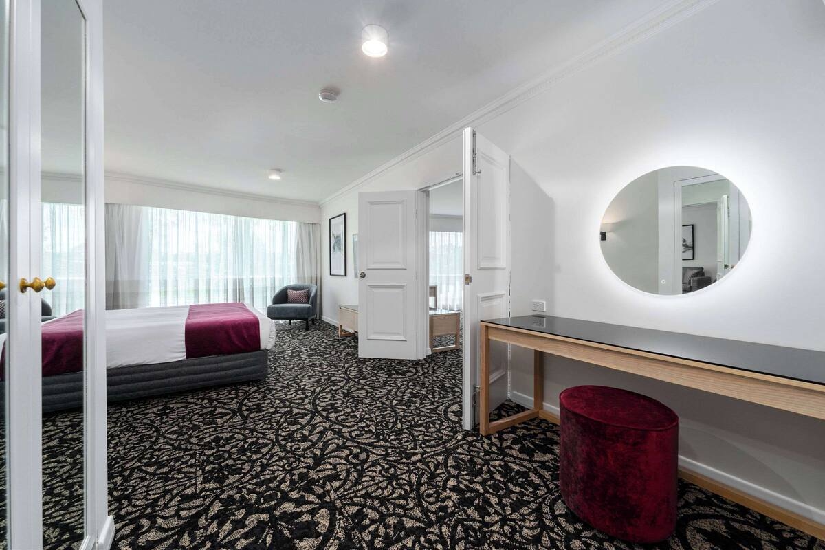 Habitación de hotel con una cama grande, un escritorio, un espejo y un cubo de basura rojo.