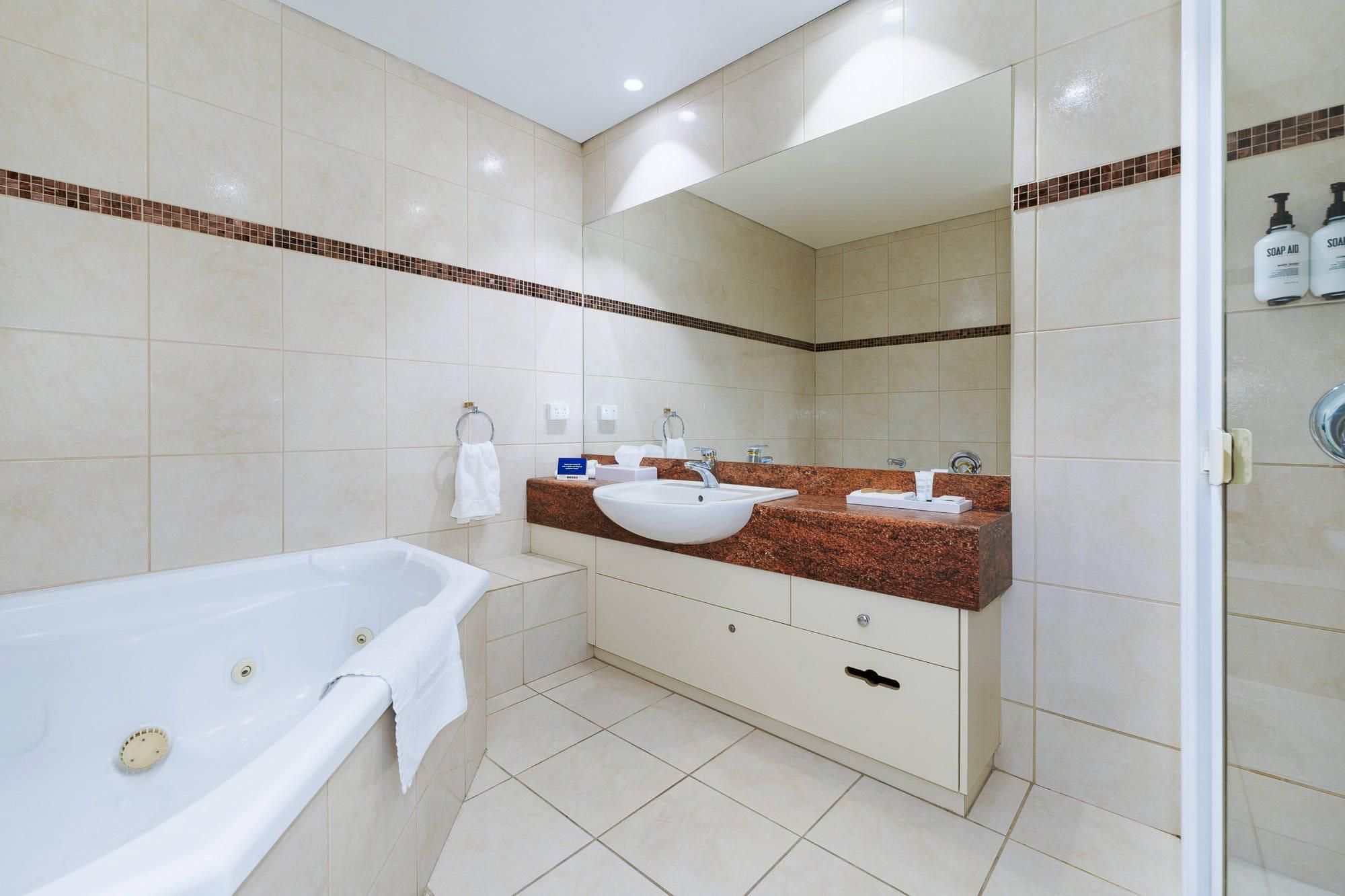 Un baño moderno con bañera, dos lavamanos, un mueble de tocador y un espejo grande.