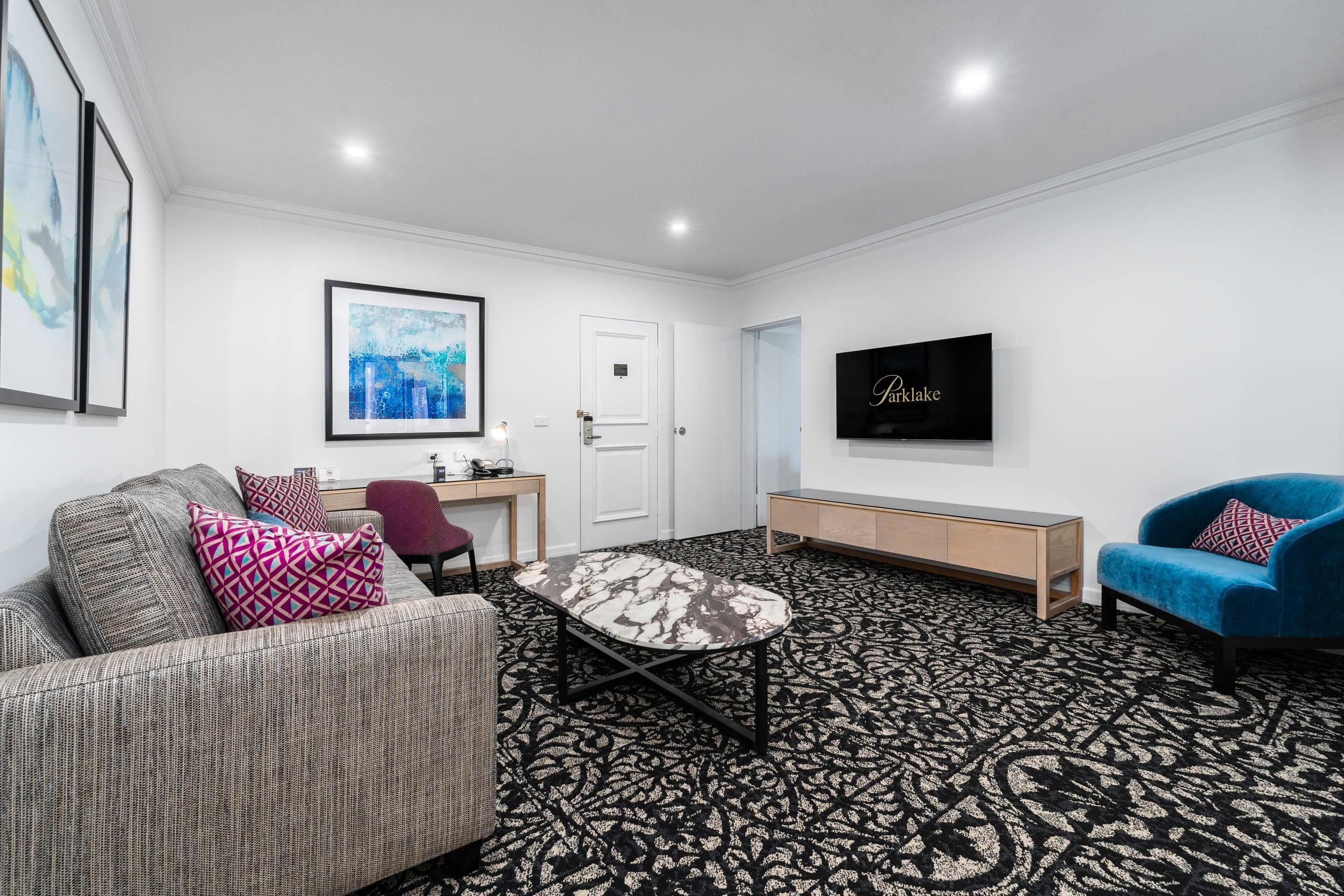 A modern living room with a sofa, a blue armchair, a coffee table, a TV, and a patterned carpet.