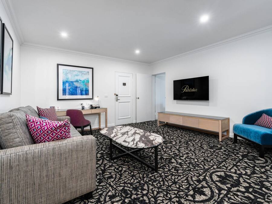 A modern living room with a sofa, a blue armchair, a coffee table, a TV, and a patterned carpet.