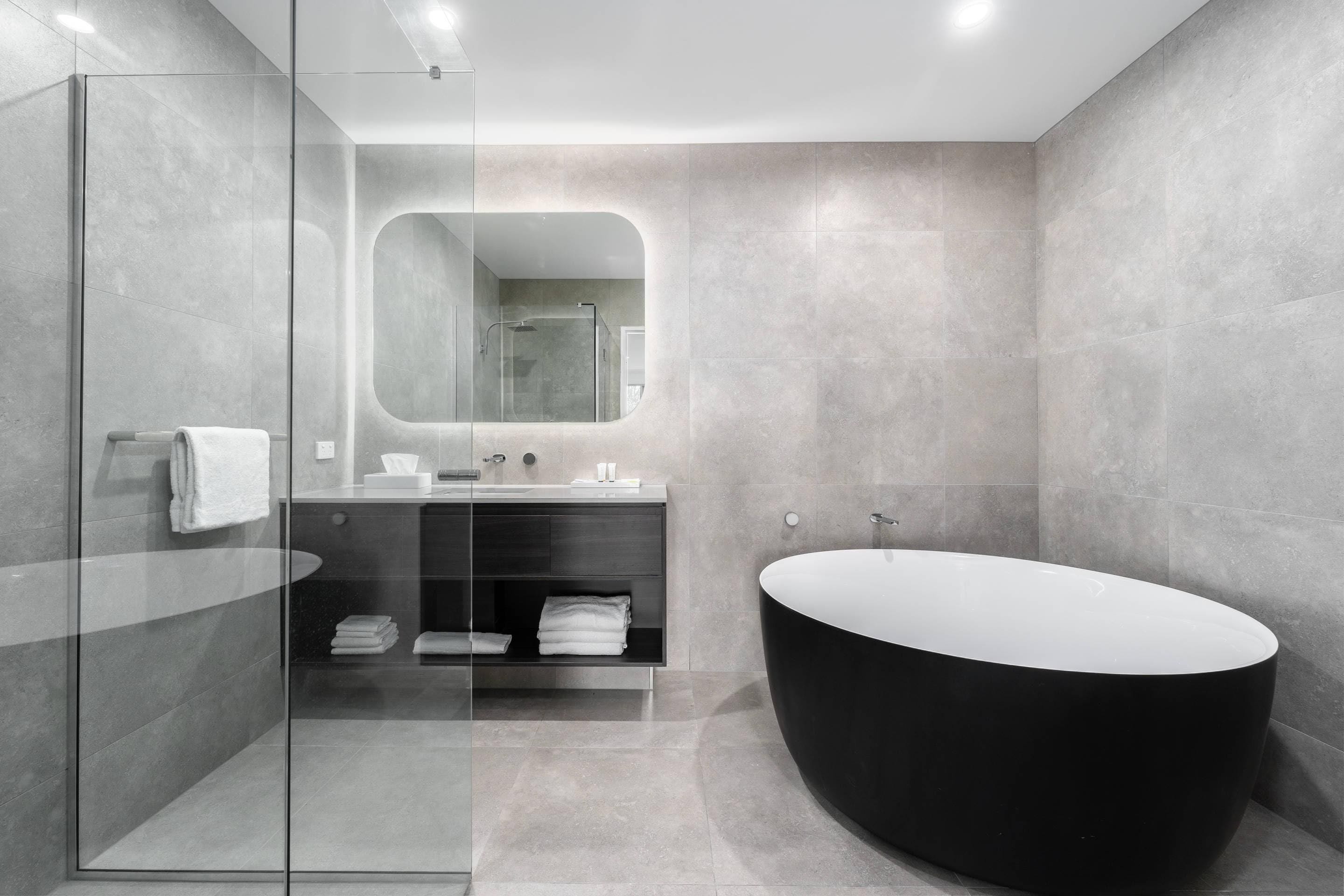 A modern bathroom with a glass-enclosed shower, a black freestanding bathtub, and a vanity with a mirror.