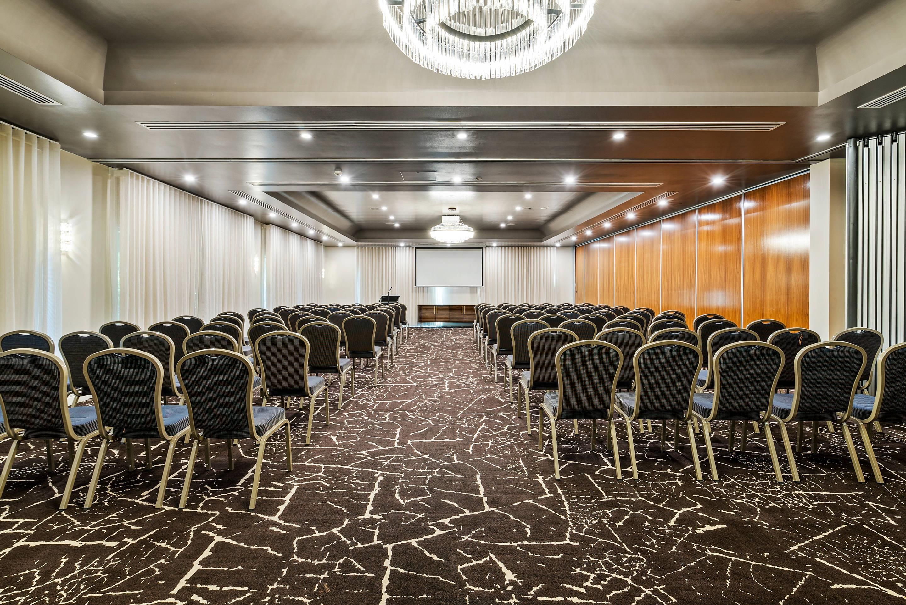 A conference room with rows of chairs, a projector screen, and a chandelier.