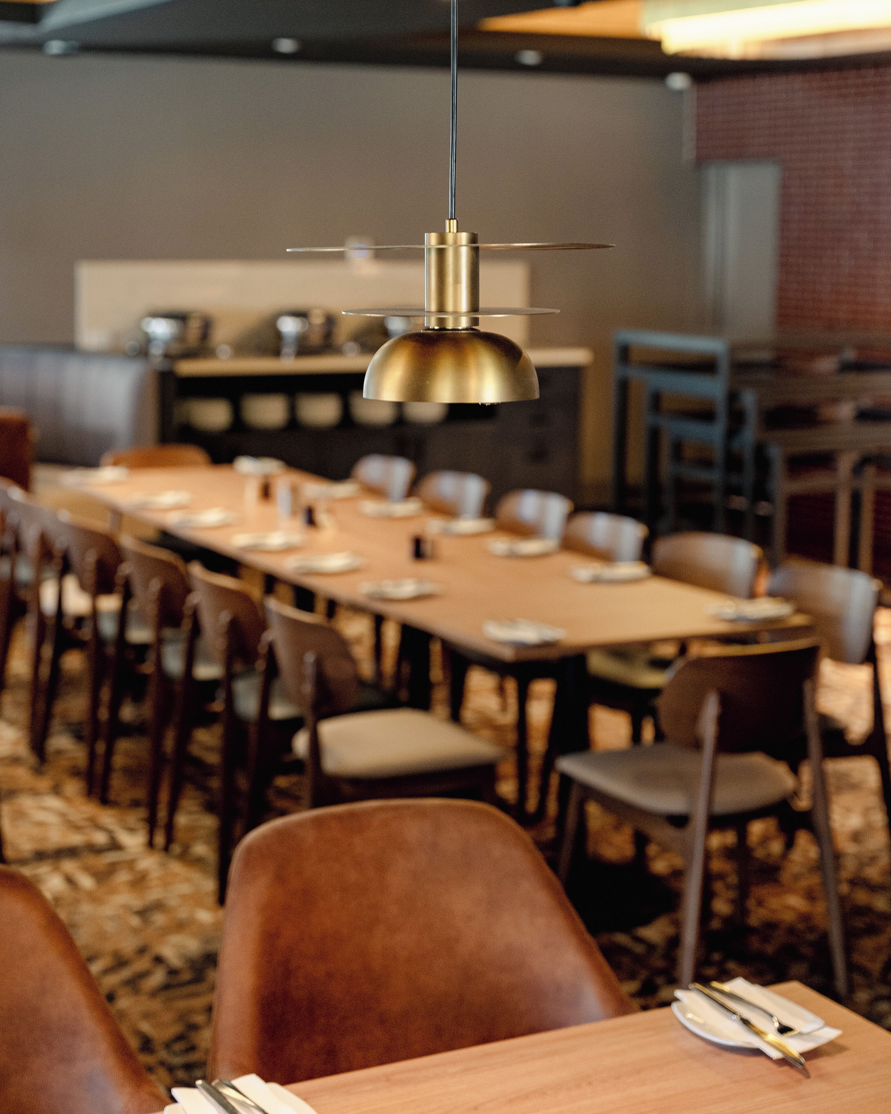 A dining area with a long table, chairs, and a hanging light fixture.