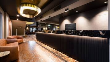 A modern lobby with a seating area, a reception desk, and a large wall-mounted TV.