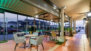 An outdoor seating area with tables and chairs, large windows, and a view of the street. - Quality Hotel Parklake Shepparton (Shepparton)