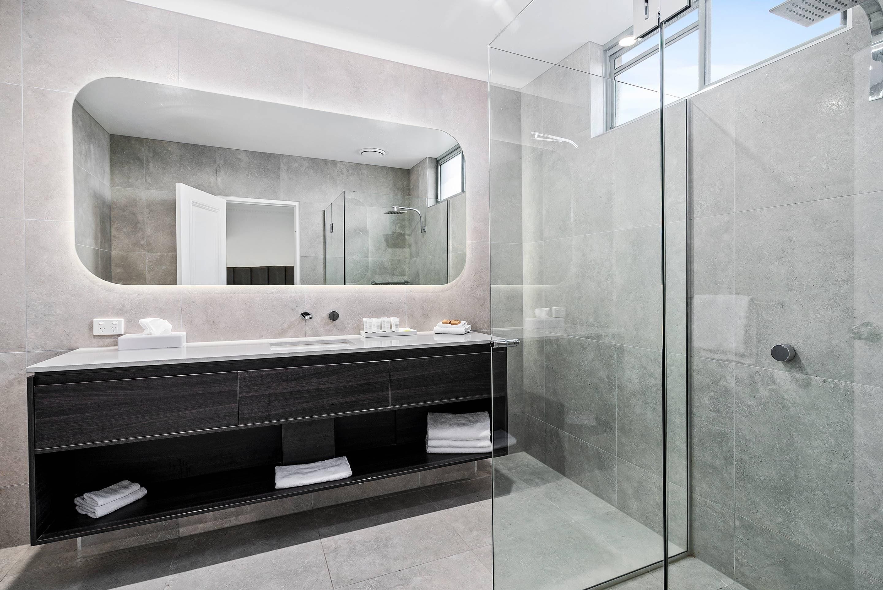A modern bathroom with a glass-enclosed shower, a large mirror, and a dark wood vanity with a towel rack.