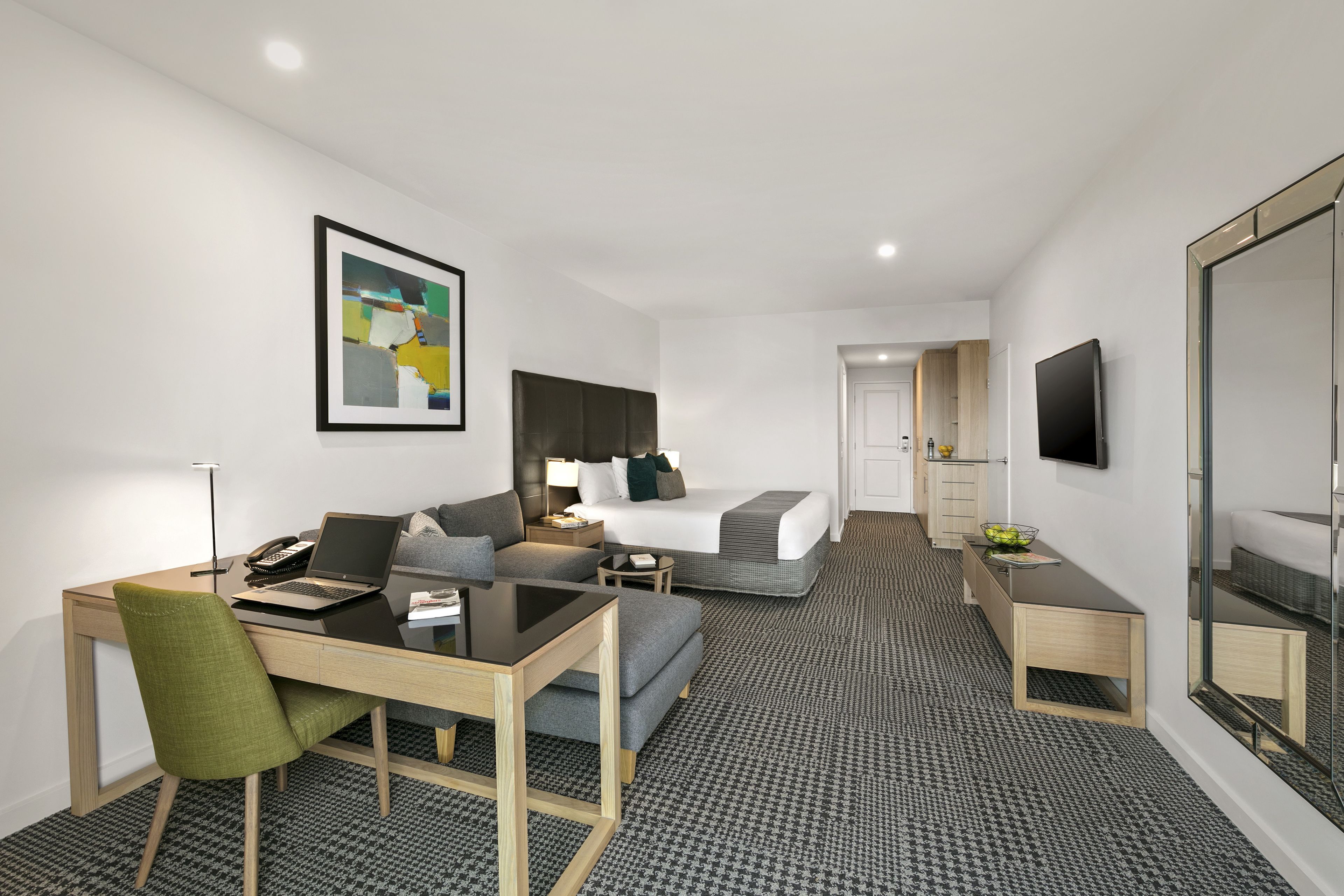 A modern hotel room with a bed, a desk, a chair, a TV, and a bathroom.