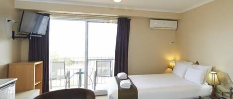 Habitación de hotel con cama, escritorio, silla, televisor y balcón con vistas.