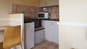 A compact kitchen with a microwave, a small refrigerator, and a chair.