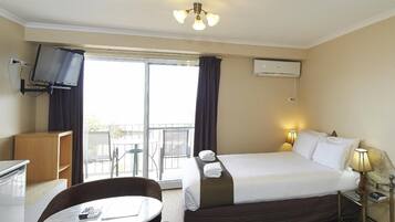 A hotel room with a bed, a desk, a chair, a TV, and a balcony with outdoor seating.