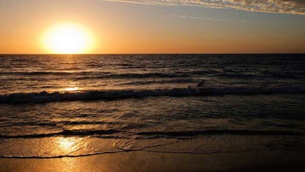 A sunset over the ocean with waves on the shore.