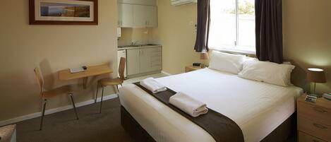 Habitación de hotel con cama, escritorio, silla, kitchenette pequeño y ventana con cortinas.