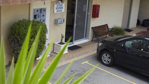 A building entrance with a reception and tour booking office sign, a parked car, and a bench outside.