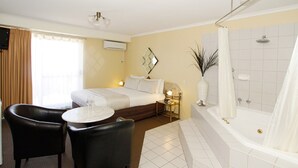 A hotel room with a bed, two chairs, a small table, a bathroom with a bathtub, and a mirror.