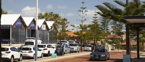 A street with parked cars and a row of buildings with signage for businesses.