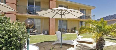 Ein Hotel mit Innenhof, inklusive Außenbestuhlung, einem großen Sonnenschirm und einer Palme.