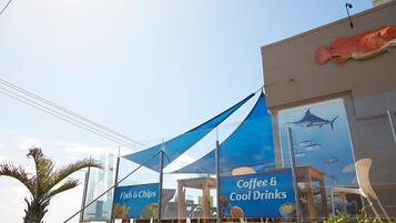 Un edificio con una gran escultura de pez en la fachada y un cartel publicitando 'Fish & Chips' y 'Coffee & Cool Drinks'.